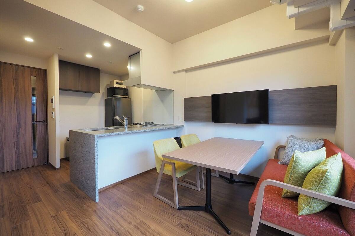 A modern kitchen with a built-in island, a dining area with a table and chairs, and a seating area with a sofa and cushions.