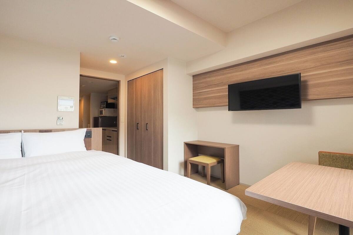 A hotel room with a bed, a desk, a TV mounted on the wall, and a wardrobe.