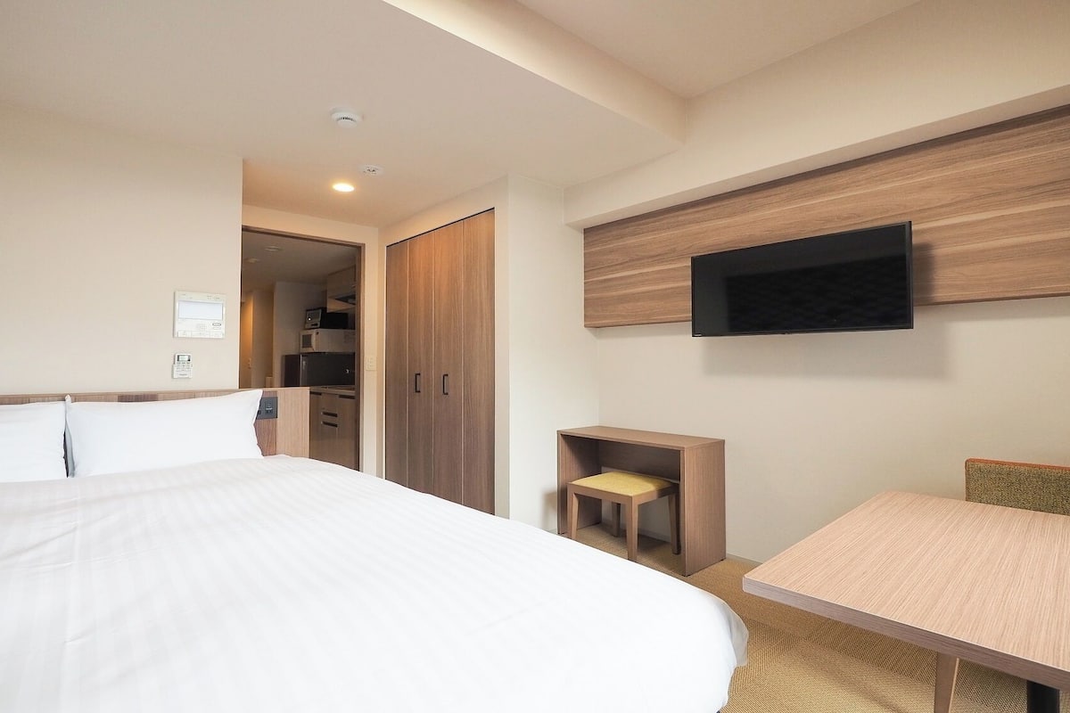 A hotel room with a bed, a desk, a TV mounted on the wall, and a wardrobe.