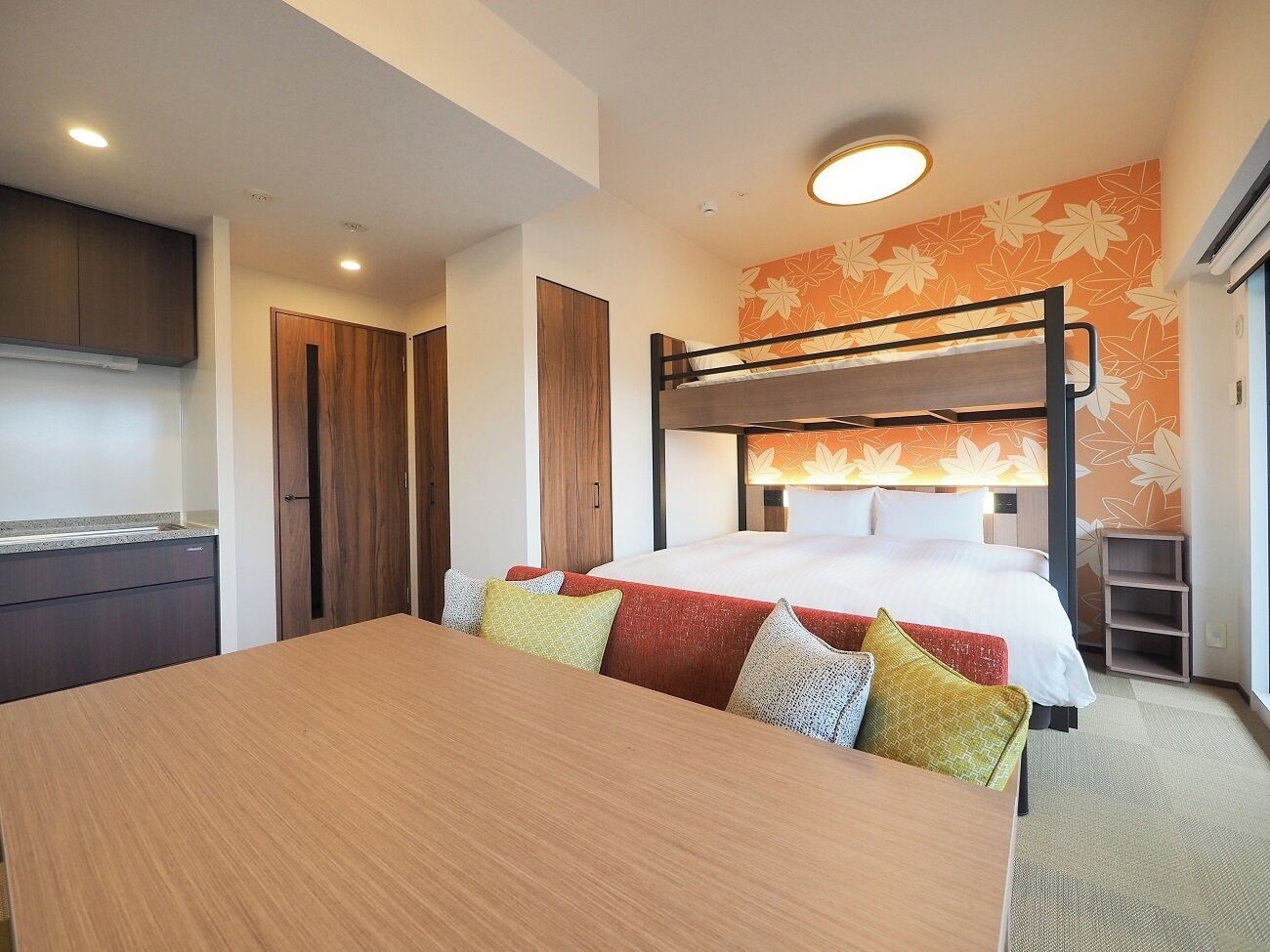A hotel room with a bunk bed, a wooden desk, and a kitchenette.