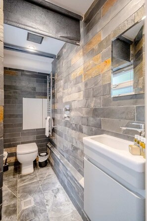 A modern bathroom with a stone wall, a white toilet, a bathtub, and a mirror.