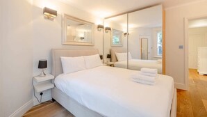 A neatly arranged bedroom with a large bed, bedside tables, and a mirror. - Gorgeous 2BD Flat With Patio - South Kensington! (London)