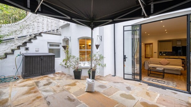 A covered outdoor area with stone flooring, a staircase, and a sliding glass door leading to a living room with a sofa and coffee table. - Gorgeous 2BD Flat With Patio - South Kensington! (London)