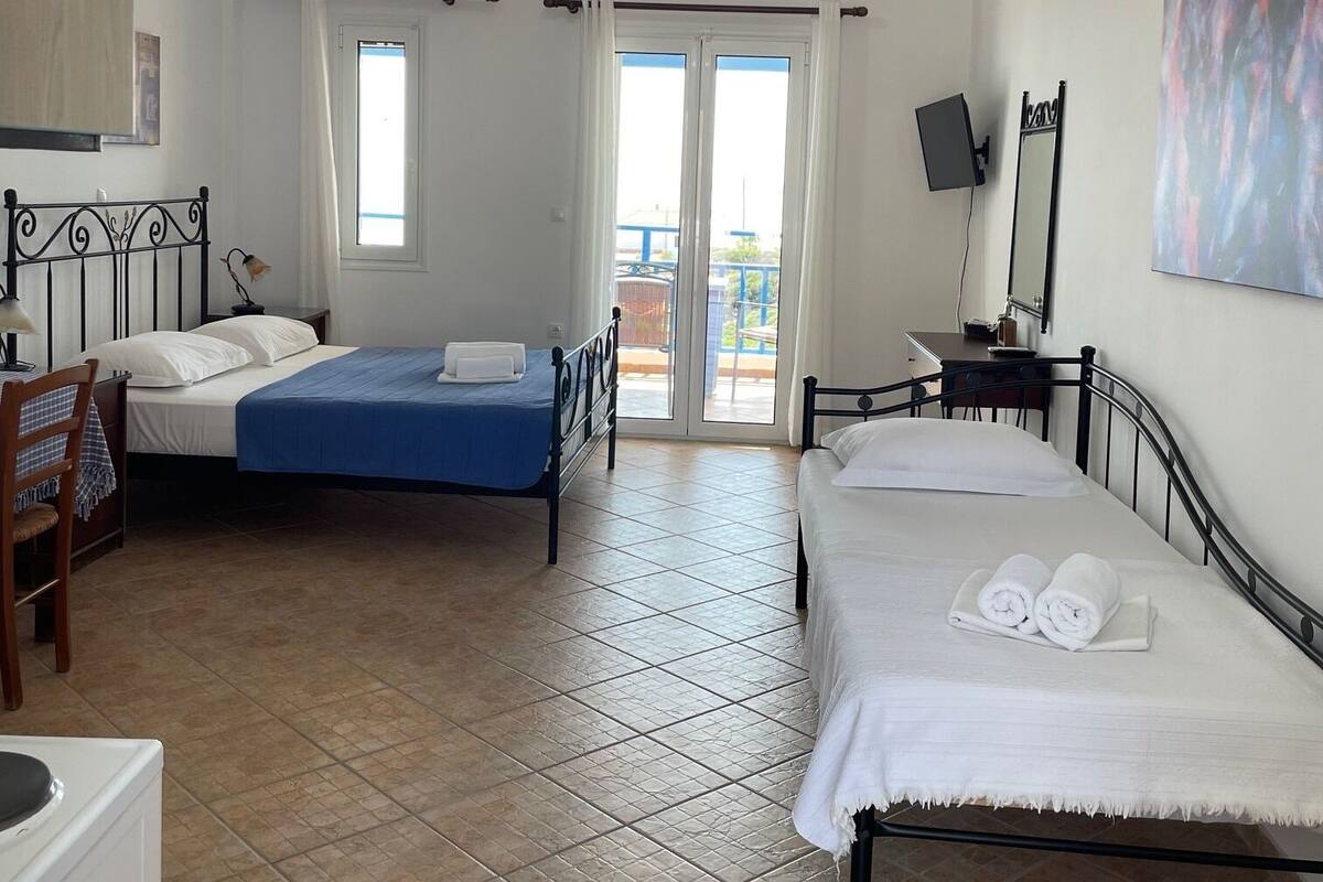 A hotel room with two beds, a desk, a chair, a TV, and a balcony with a view.
