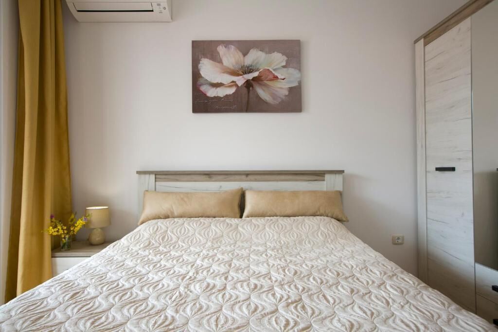 A bedroom with a bed, a nightstand, a lamp, a painting, and a wardrobe.
