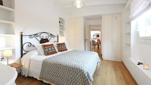 Una camera da letto con un letto, un comodino e una lampada. Si vede un armadio e una porta che dà su un'altra stanza.