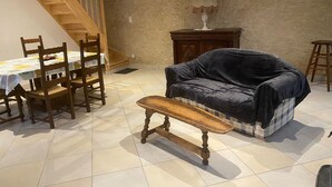 Ein gemütliches Wohnzimmer mit einem Holzesstisch, Stühlen, einer Couch und einer Bank. Eine Treppe führt zu einer oberen Ebene.