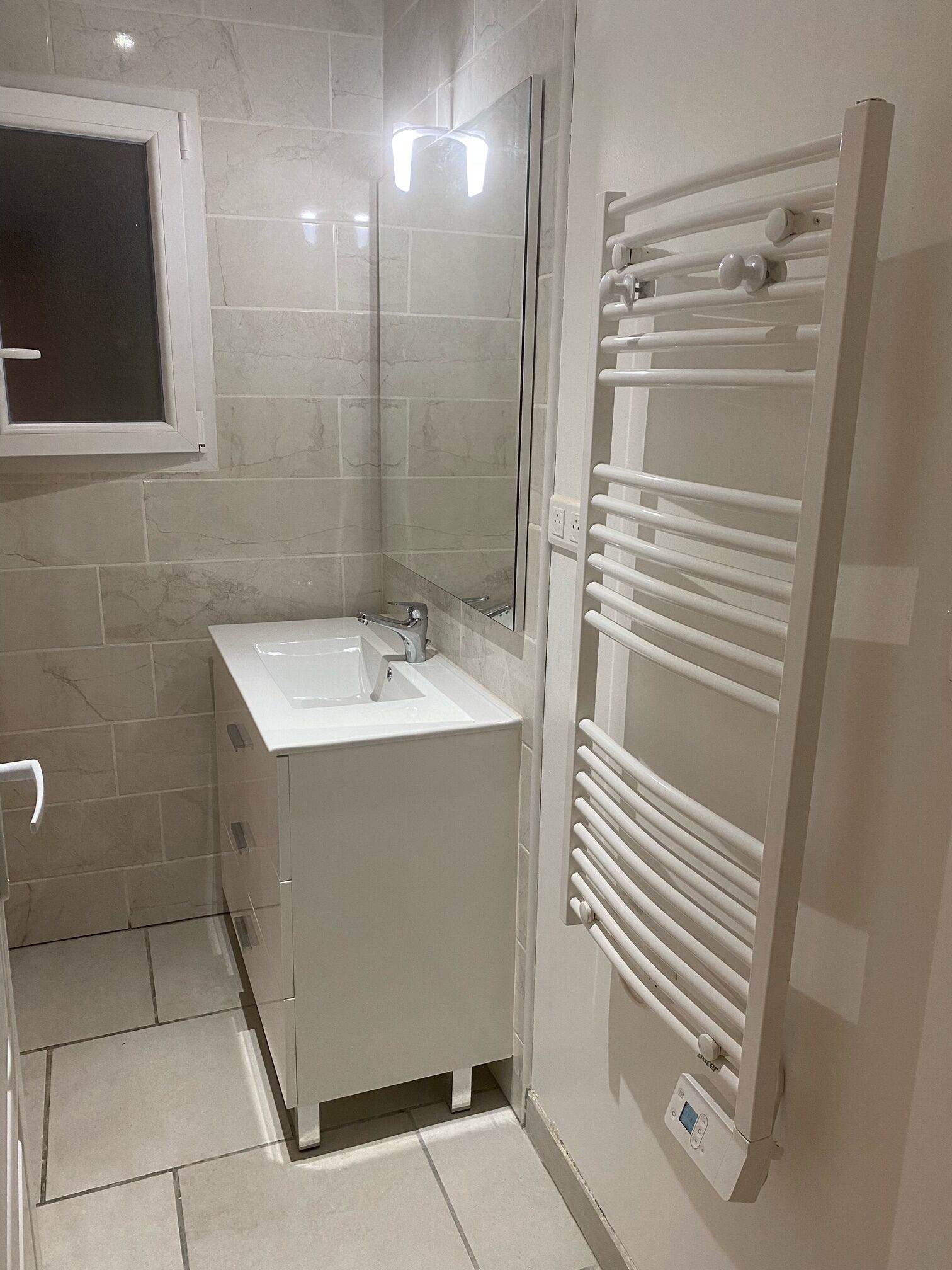 A modern bathroom with a white sink, mirror, and built-in towel rack.
