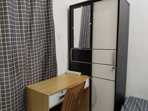 Une petite pièce avec un bureau en bois, une chaise, un rideau à carreaux noirs et blancs et un miroir sur la porte.