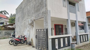 Un immeuble de deux étages avec une façade en béton, un balcon et une entrée fermée par un portail.
