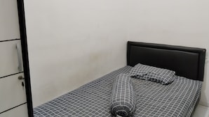 Une petite chambre avec un lit simple, un mur blanc uni et une tête de lit noire.