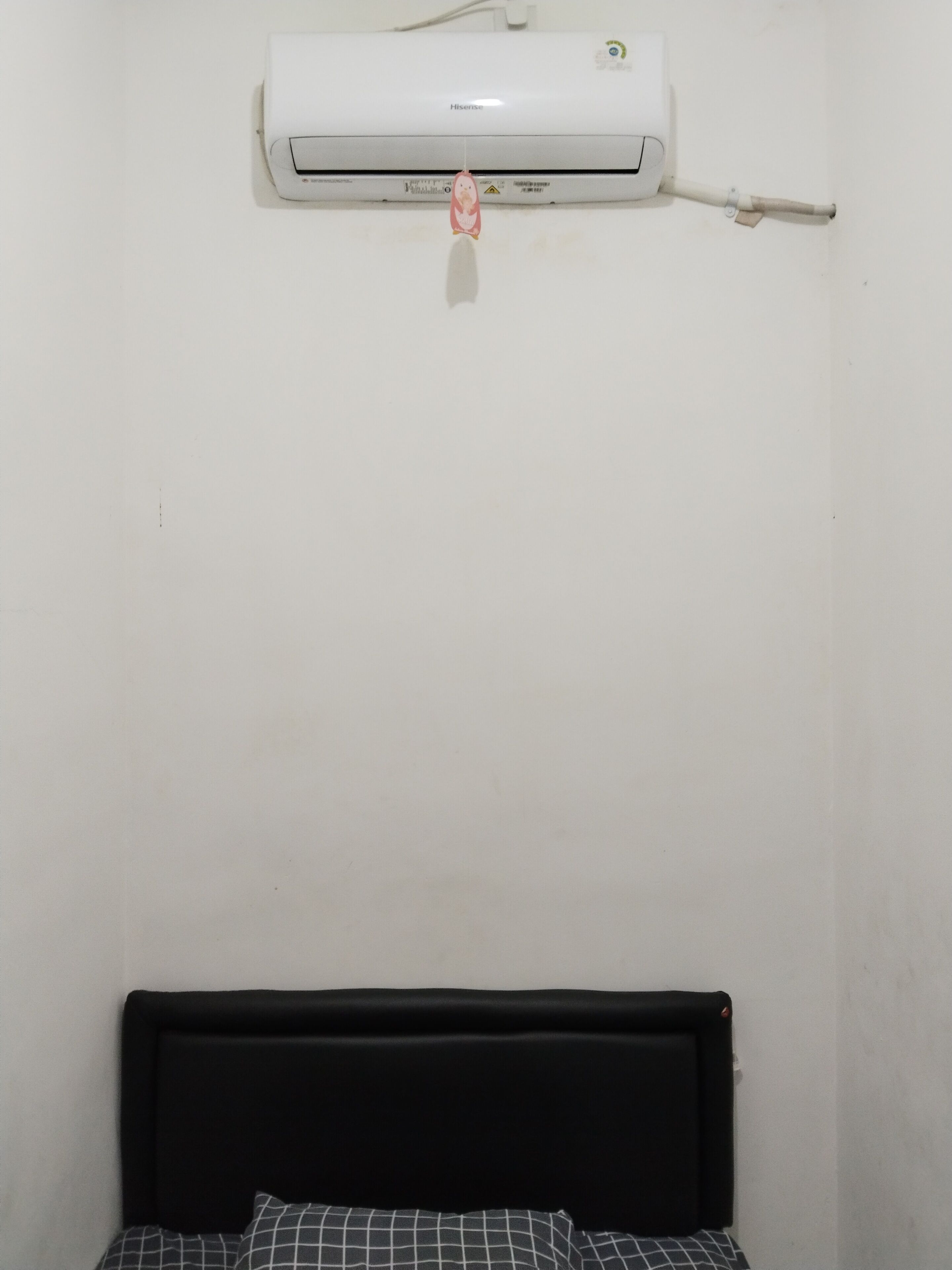 A room with a bed, a wall-mounted air conditioner, and a visible electrical outlet.
