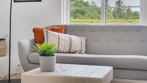 Uma sala de estar moderna com um sofá cinzento, uma planta em vaso e uma mesa de centro com ladrilhos.