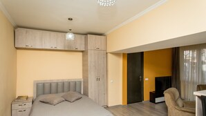 A bedroom with a bed, a nightstand, a wardrobe, a chair, and a television. - HB apartments Opera II (Tbilisi)