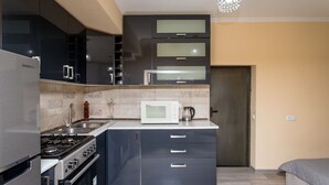 A modern kitchen with a built-in microwave, stove, and oven, and a separate refrigerator. - HB apartments Opera II (Tbilisi)