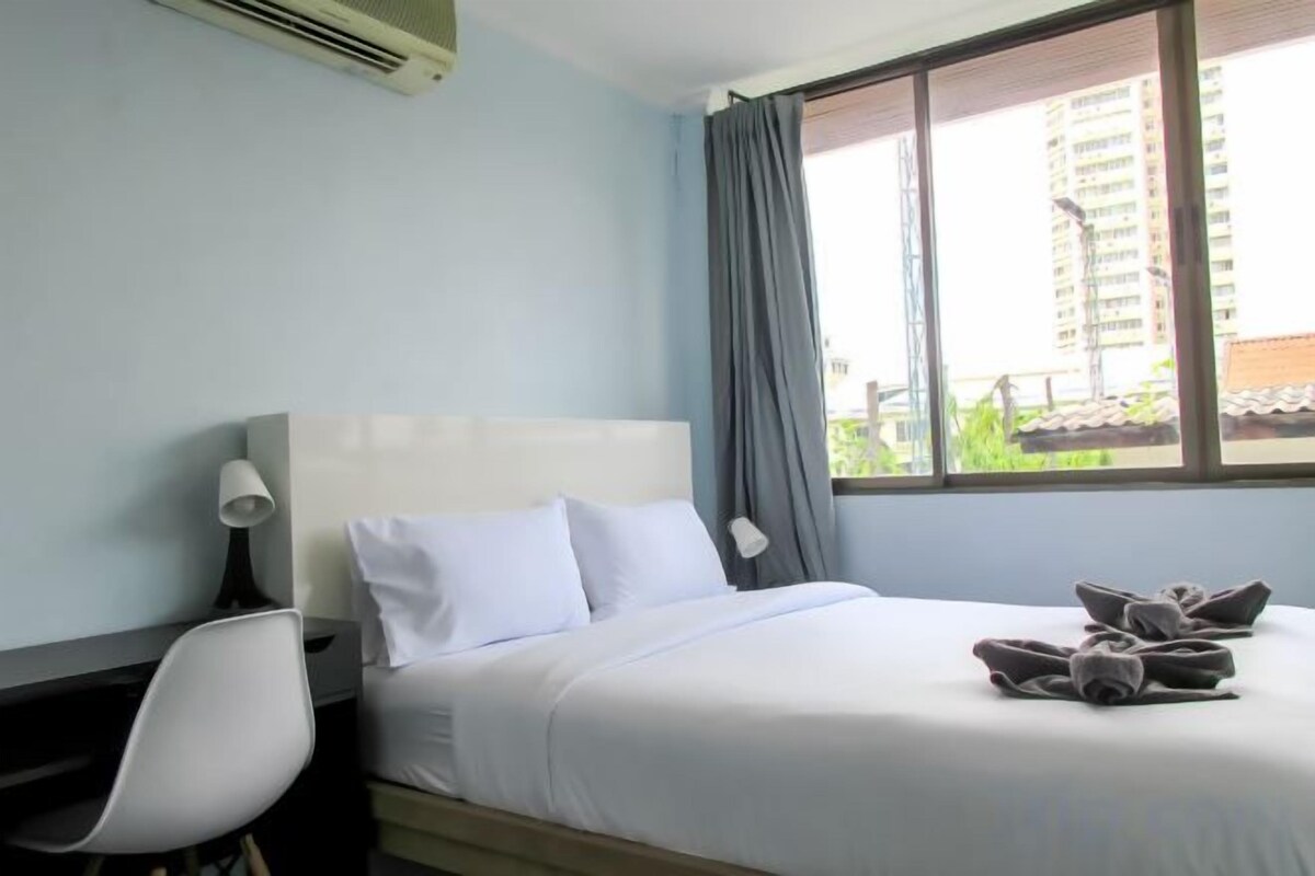Une chambre d’hôtel avec un lit, un bureau, une chaise et une fenêtre avec des rideaux.