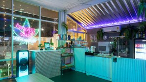 Ein modernes Café mit einer Neonreklame, einem Holztisch und verschiedenen Pflanzen sowie Küchengeräten.