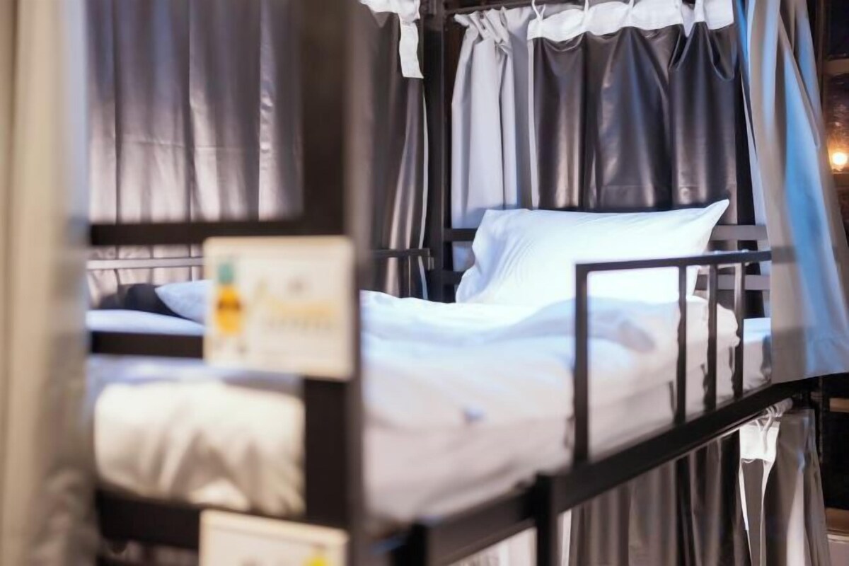 Un lit superposé avec un matelas et des oreillers blancs, une structure en métal et des rideaux.