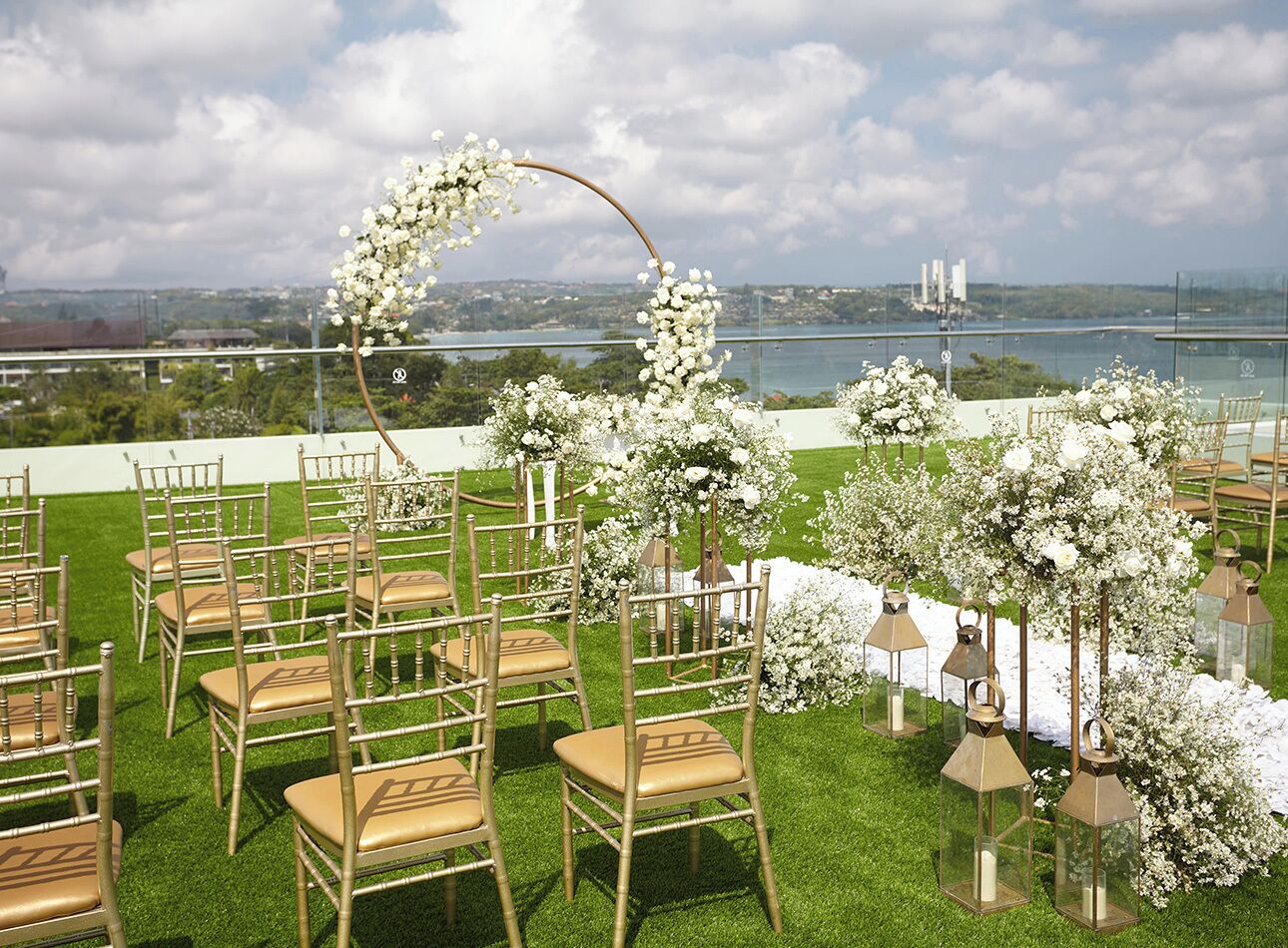 An outdoor wedding setup with chairs arranged in rows, a floral arch, and lanterns.