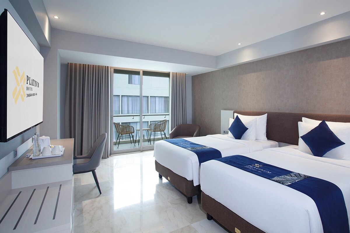 Habitación de hotel con dos camas, un escritorio, una silla y una televisión.