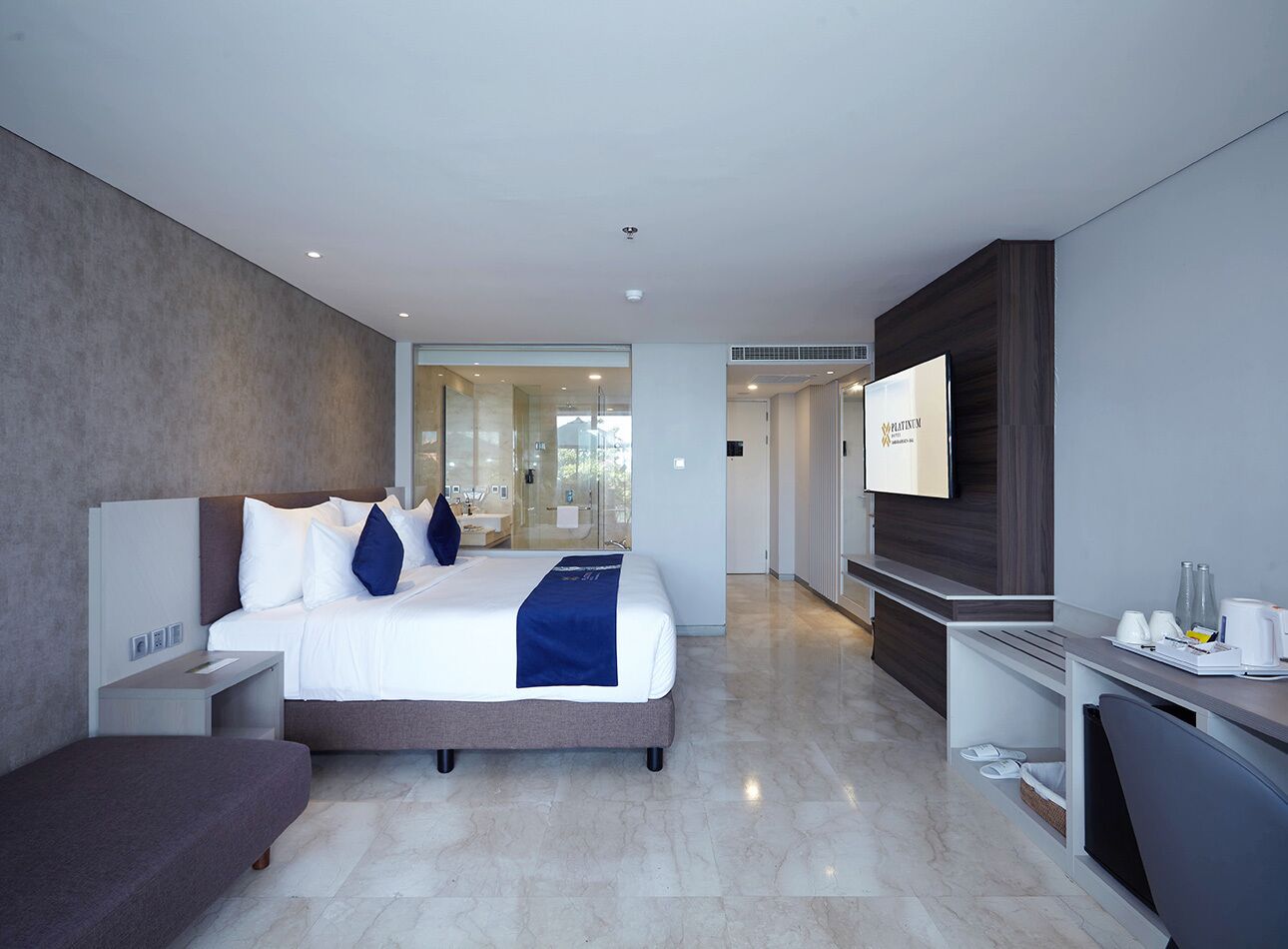 A modern hotel room with a large bed, a desk, a flat-screen TV, and a glass shower area.