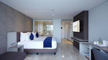 A modern hotel room with a large bed, a desk, a flat-screen TV, and a glass shower area.