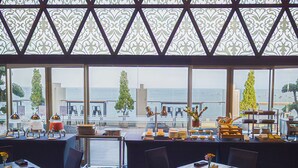 Un restaurante con mesas y sillas, vistas al mar y un techo con diseño.