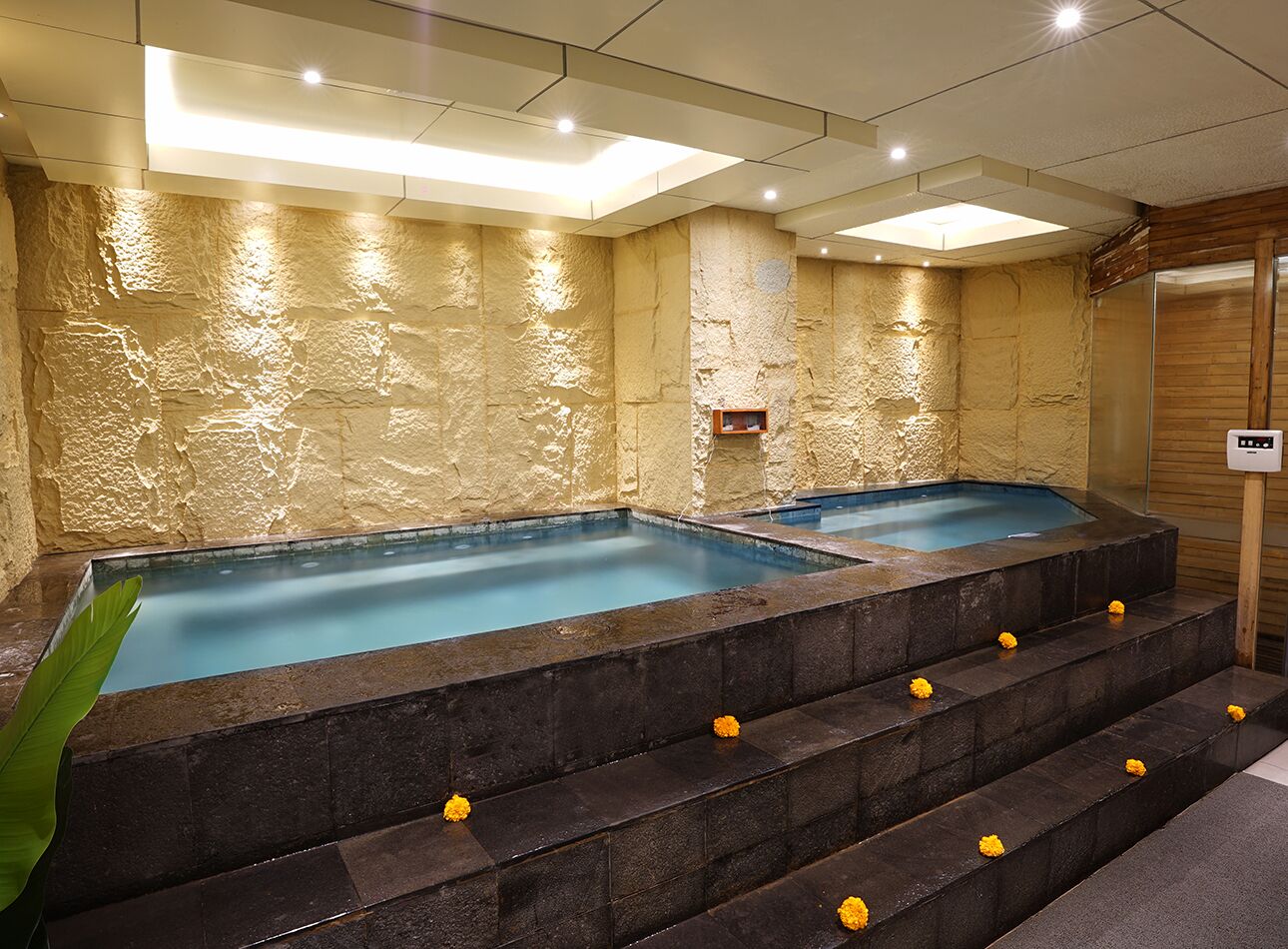 Un área de spa con dos jacuzzis, paredes de piedra y un panel de madera a la derecha.