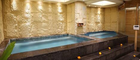 A spa area with two hot tubs, stone walls, and a wooden panel on the right.