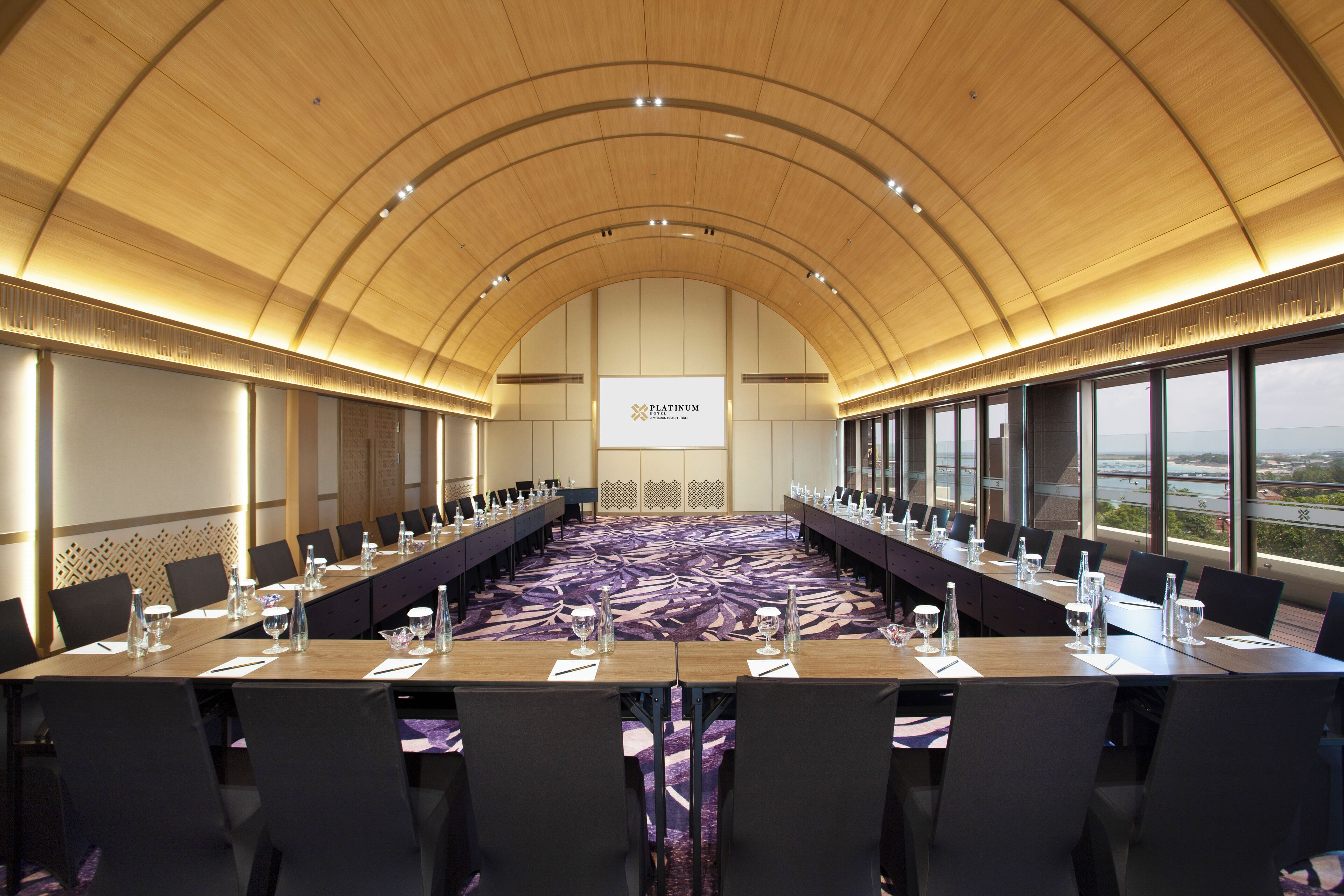A conference room with a long table, chairs, and a large screen at the front.
