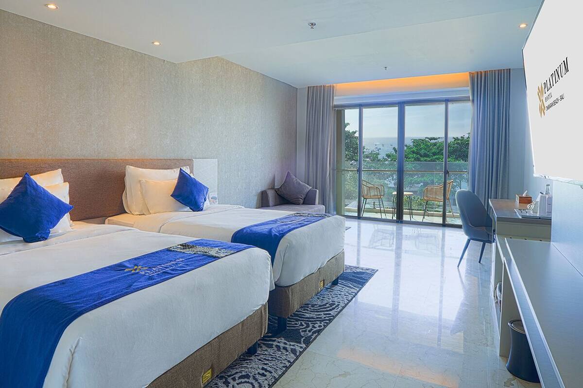 A hotel room with two beds, a desk, and a balcony with a view.