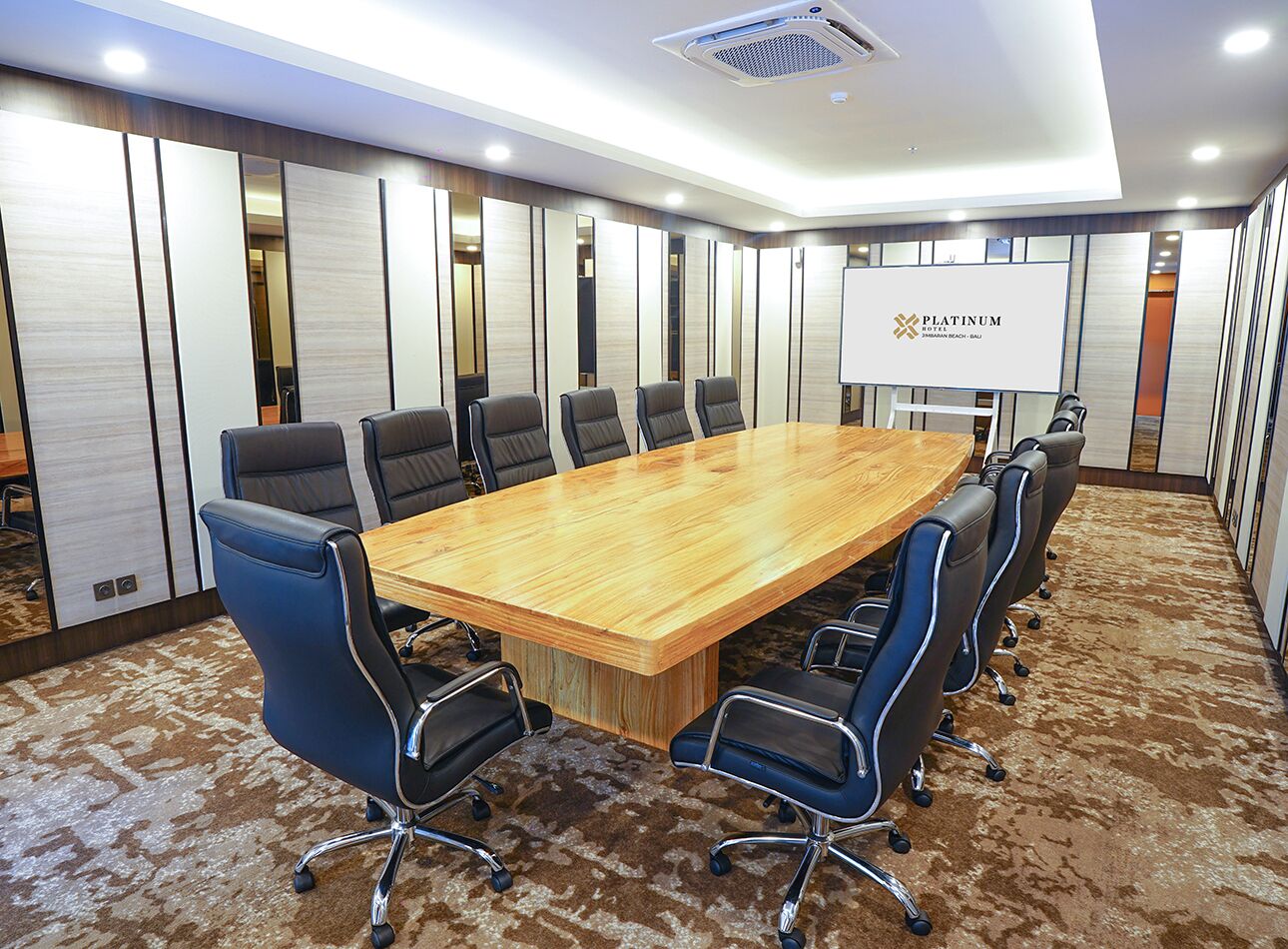 Une salle de conférence dotée d’une grande table en bois, de chaises noires et d’un sol recouvert de moquette.