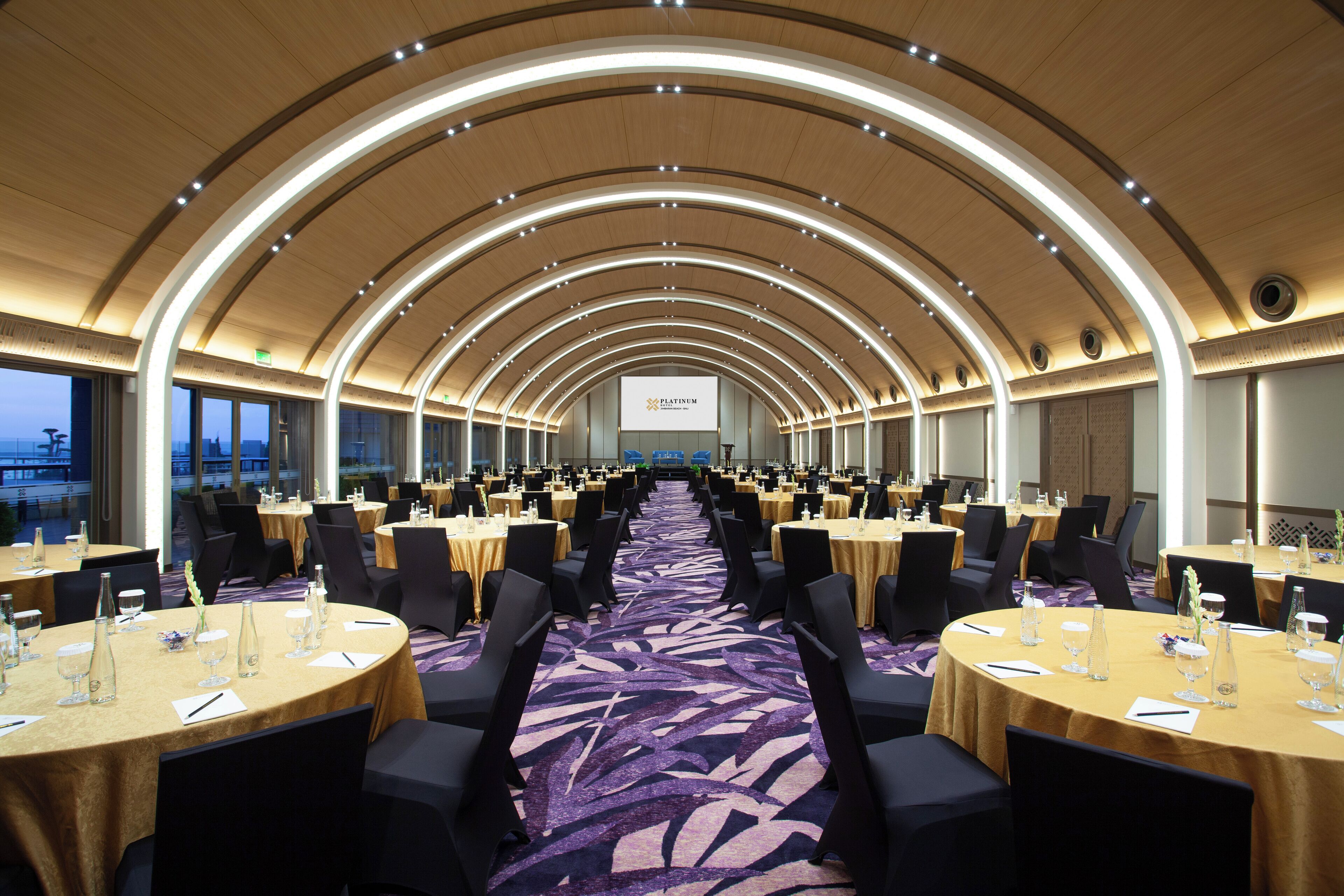 A conference room with round tables, black chairs, and a purple carpet.