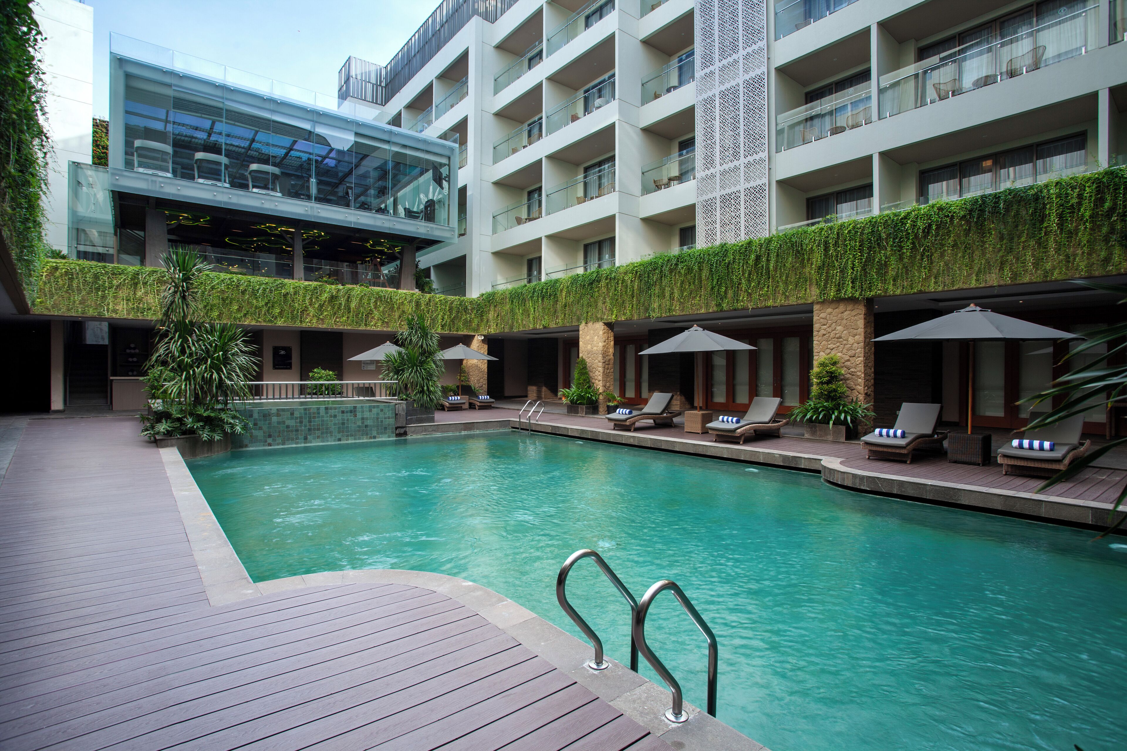 Un hotel moderno con piscina en la azotea, sillas de descanso y una terraza con paredes de vidrio.