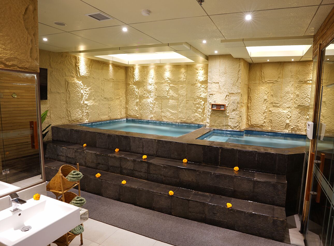 A spa area with two hot tubs, a staircase leading to a seating area, and a white sink with a mirror.