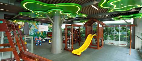 A children's play area with wooden climbing structures, a yellow slide, and a climbing net.