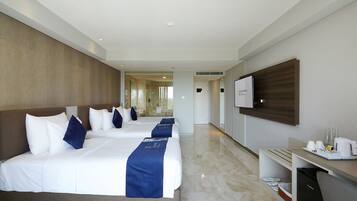 Habitación de hotel con dos camas, un escritorio, un televisor y un baño visible a través de una puerta de cristal.