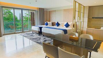 A modern hotel room with a large bed, a glass dining table, and a view of greenery through the sliding doors.