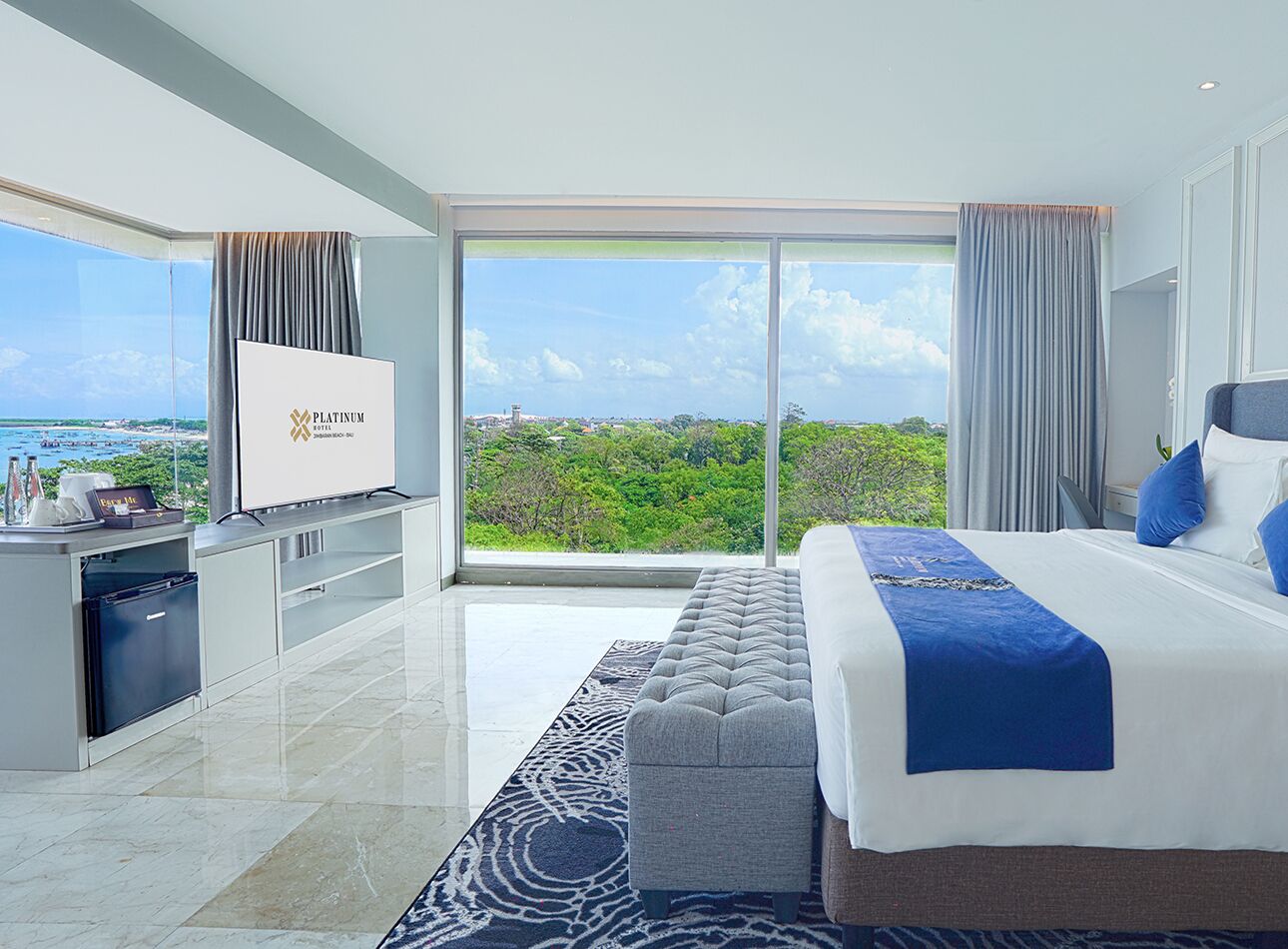 Habitación de hotel moderna con una cama grande, televisión, minibar y vistas al exterior.