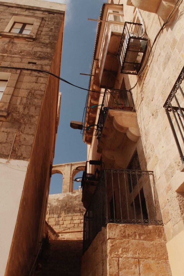 Un estrecho callejón entre edificios con fachadas de piedra y barandillas de metal en los balcones.