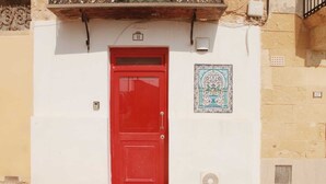A red door with a small window above it, a decorative tile on the wall, and a number '11' sign. - Barakka Garden Studio  (Valletta)