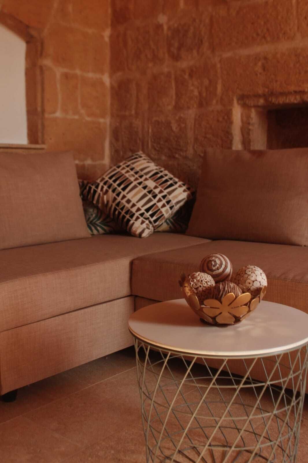 A cozy living room with a brown sofa, a patterned throw pillow, and a round metal table with a decorative bowl.