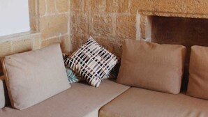 A cozy room with a stone wall, a fireplace, and a beige sectional sofa with patterned cushions. - Barakka Garden Studio  (Valletta)
