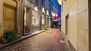 A cobblestone street with buildings on either side, a café with outdoor seating, and a street lamp. - Modern Loft with Washer, TV & Near Attractions (Ville-Haute)