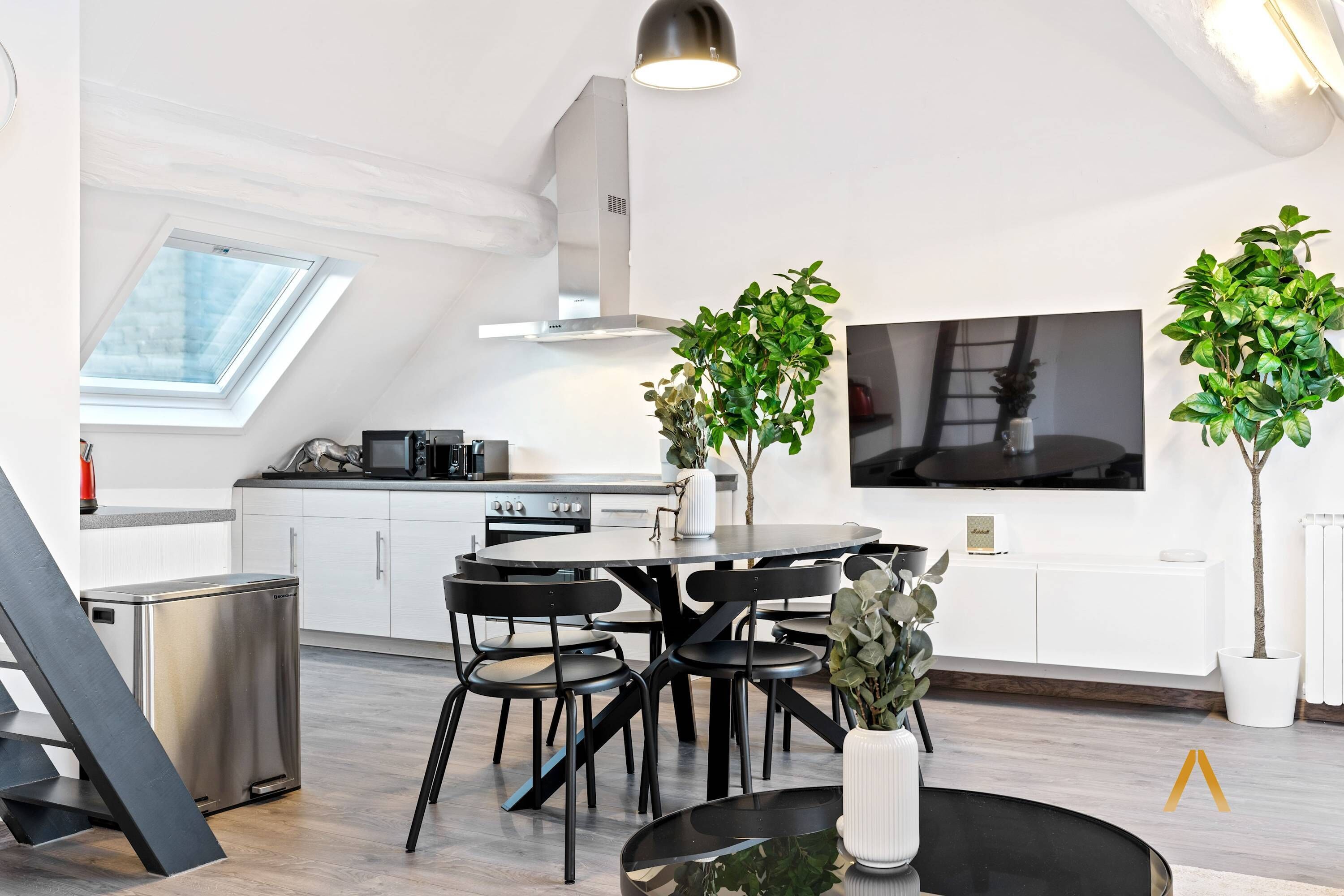 Una cocina moderna con comedor, que incluye un tragaluz, un televisor grande y plantas en macetas.