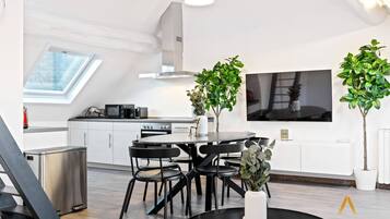 Una cocina moderna con comedor, que incluye un tragaluz, un televisor grande y plantas en macetas.
