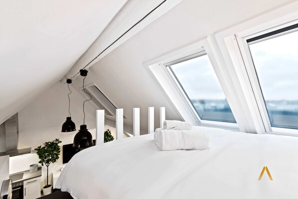 A modern bedroom with a skylight, a neatly made bed, and a view of the outdoors.