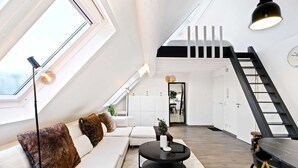 A modern loft apartment with a loft bed, a staircase, a dining area, and a living room with a sofa and coffee table. - Modern Loft with Washer, TV & Near Attractions (Ville-Haute)