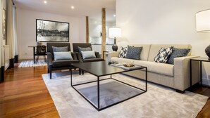 Un salon moderne avec un canapé, deux fauteuils, une table basse et un grand tableau accroché au mur.
