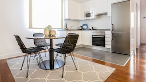 A modern kitchen with white cabinets, a stainless steel refrigerator, a microwave, and a stove. There is a dining table with four chairs and a decorative vase. - Superior 2 Bedroom Apartment - Chueca (Chueca)